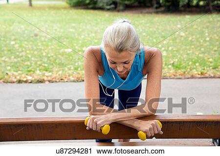 Stock Image - Mature woman taking a break at park bench whilst training in park. Fotosearch
