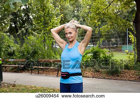 Mature woman tying up hair whilst training in park View Large Photo Image Picture - Mature woman tying up hair whilst training in park. Fotosearch
