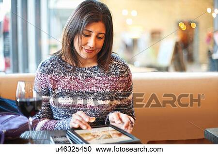 Stock Image - Mature woman using touchscreen on digital tablet in wine bar. Fotosearch