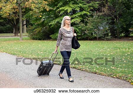 Mature woman walking through park pulling wheeled suitcase View Large Photo Image Stock Image - Mature woman walking through park pulling wheeled suitcase. Fotosearch