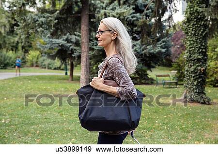 Stock Photo - Mature woman walking through park carrying shoulder bag. Fotosearch