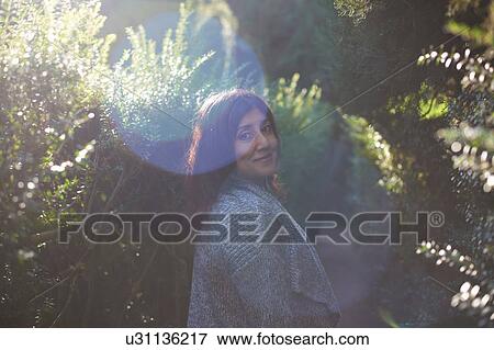 Stock Photo - Mature woman wearing cardigan looking over shoulder at camera smiling. Fotosearch