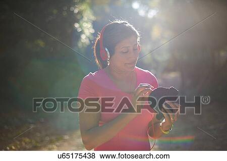 Mature woman wearing headphones looking down preparing armband View Large Photo Image Stock Photo - Mature woman wearing headphones looking down preparing armband. Fotosearch