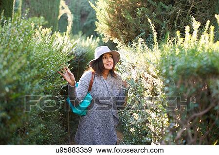 Mature woman wearing sunhat and cardigan touching plants, looking away smiling, Seville, Spain View Large Photo Image Stock Photo - Mature woman wearing sunhat and cardigan touching plants, looking away smiling, Seville, Spain. Fotosearch