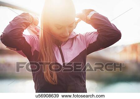 Stock Photo - Mid adult female runner adjusting tracksuit hood on footbridge. Fotosearch
