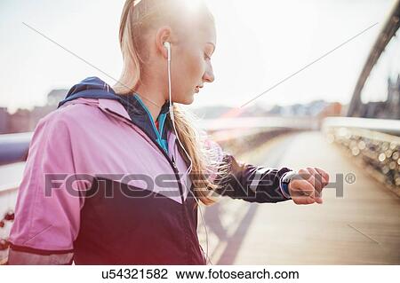 Stock Image - Mid adult female runner checking time on footbridge. Fotosearch