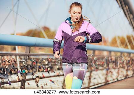 Mid adult female runner checking time whilst running across bridge View Large Photo Image Stock Photo - Mid adult female runner checking time whilst running across bridge. Fotosearch