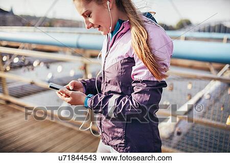 Mid adult female runner choosing smartphone music on footbridge View Large Photo Image Stock Image - Mid adult female runner choosing smartphone music on footbridge. Fotosearch