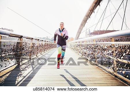 Picture - Mid adult female runner running across footbridge. Fotosearch