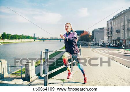 Stock Photo - Mid adult female runner running along riverside. Fotosearch