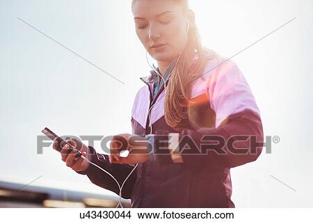 Picture - Mid adult female runner wearing earphones checking time on smartwatch. Fotosearch
