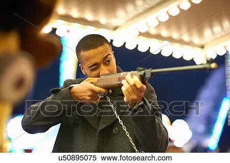 Mid adult man aiming rifle at shooting gallery at funfair View Large Photo Image Stock Photography - Mid adult man aiming rifle at shooting gallery at funfair. Fotosearch