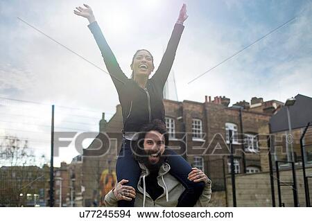Picture - Mid adult man carrying young woman on shoulders, smiling. Fotosearch