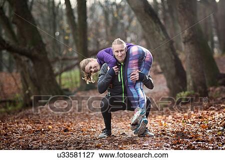 Stock Photo - Mid adult man crouching in forest carrying young woman on shoulders looking at camera smiling. Fotosearch