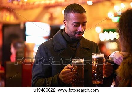 Mid adult man handing young woman glass of beer, looking down smiling View Large Photo Image Stock Image - Mid adult man handing young woman glass of beer, looking down smiling. Fotosearch