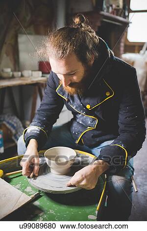 Mid adult man sitting at pottery wheel looking down at clay pot View Large Photo Image Stock Image - Mid adult man sitting at pottery wheel looking down at clay pot. Fotosearch