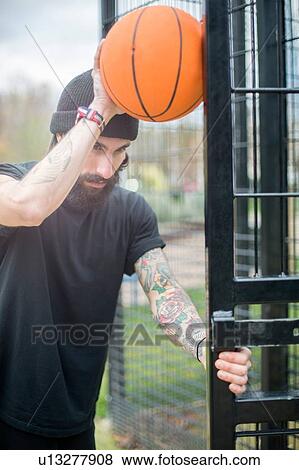 Mid adult man standing by fence, holding basketball against fence, pensive expression View Large Photo Image Stock Photo - Mid adult man standing by fence, holding basketball against fence, pensive expression. Fotosearch