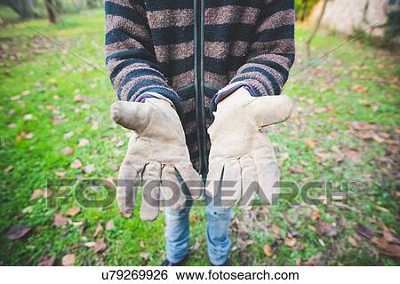 Stock Photograph - Mid adult man wearing striped cardigan and protective gloves, hands open. Fotosearch