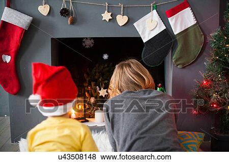 Stock Photo - Mid adult mother and toddler son preparing christmas fireplace. Fotosearch