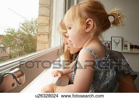 Picture - Mid adult woman and toddler daughter gazing out from living room window. Fotosearch