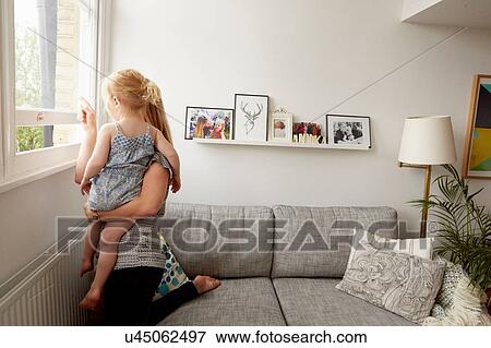 Mid adult woman and toddler daughter looking from living room window View Large Photo Image Stock Photo - Mid adult woman and toddler daughter looking from living room window. Fotosearch