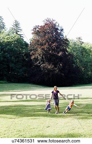 Mid adult woman and two daughters holding hands and running in park View Large Photo Image Stock Image - Mid adult woman and two daughters holding hands and running in park. Fotosearch