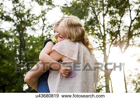 Mid adult woman carrying sleeping daughter in park View Large Photo Image Stock Photo - Mid adult woman carrying sleeping daughter in park. Fotosearch