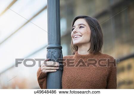 Stock Photograph - Mid adult woman holding city lamppost. Fotosearch