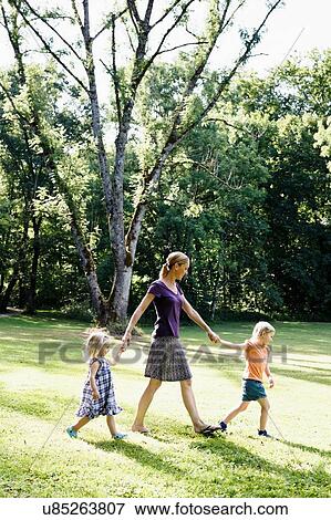 Mid adult woman holding hands with two daughters in park View Large Photo Image Stock Photo - Mid adult woman holding hands with two daughters in park. Fotosearch