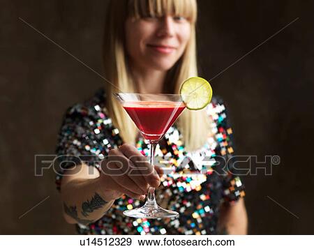 Stock Photo - Mid adult woman holding raw juice in cocktail glass garnished with lime slice looking at camera smiling. Fotosearch