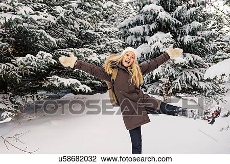 Mid adult woman in front of snow covered evergreen tree standing on one leg arms raised looking at camera smiling View Large Photo Image Stock Image - Mid adult woman in front of snow covered evergreen tree standing on one leg arms raised looking at camera smiling. Fotosearch