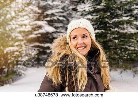 Stock Photo - Mid adult woman in front of snow covered trees looking away smiling. Fotosearch