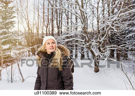 Stock Photo - Mid adult woman in front of snow covered trees looking away smiling. Fotosearch