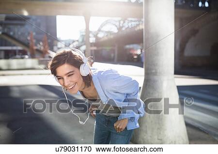 Mid adult woman laughing whilst listening to headphones in city View Large Photo Image Stock Image - Mid adult woman laughing whilst listening to headphones in city. Fotosearch