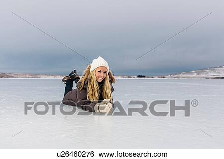 Stock Photograph - Mid adult woman lying on front on frozen lake looking at camera smiling. Fotosearch