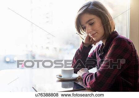 Mid adult woman reading digital tablet at cafe window seat View Large Photo Image Stock Photo - Mid adult woman reading digital tablet at cafe window seat. Fotosearch