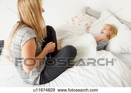 Mid adult woman sitting on bed with toddler daughter at bedtime View Large Photo Image Stock Photo - Mid adult woman sitting on bed with toddler daughter at bedtime. Fotosearch