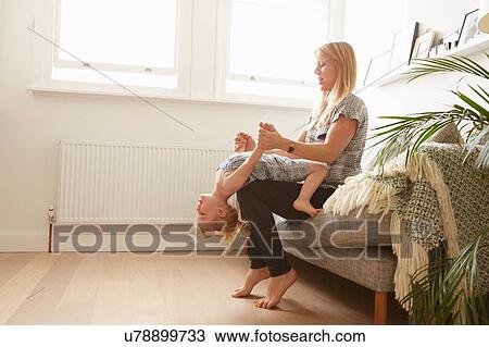 Mid adult woman sitting on sofa playing with toddler daughter View Large Photo Image Stock Image - Mid adult woman sitting on sofa playing with toddler daughter. Fotosearch