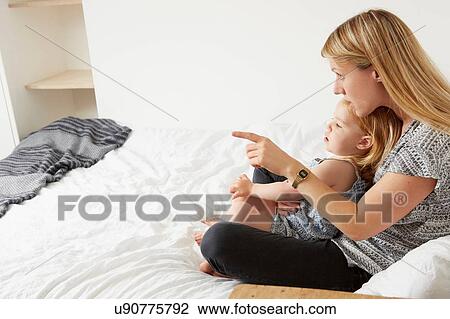 Mid adult woman sitting with toddler daughter on bed View Large Photo Image Stock Image - Mid adult woman sitting with toddler daughter on bed. Fotosearch