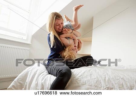 Stock Photo - Mid adult woman turning toddler daughter upside down on bed. Fotosearch