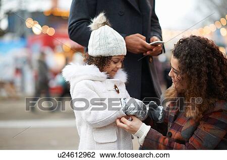 Stock Image - Mother crouching helping daughter put on mittens. Fotosearch