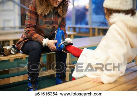 Picture - Mother sitting on bench helping daughter to put on ice skates. Fotosearch