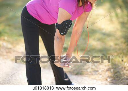 Stock Image - Neck down of mature woman wearing wristband, hands together bending over stretching. Fotosearch