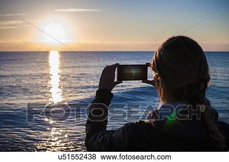 Over shoulder silhouetted view of young woman photographing sunset over sea, Villasimius, Sardinia, Italy View Large Photo Image Stock Photo - Over shoulder silhouetted view of young woman photographing sunset over sea, Villasimius, Sardinia, Italy. Fotosearch