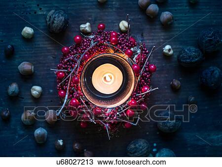 Stock Image - Overhead view of burning candle surrounded by berry wreath and nuts. Fotosearch