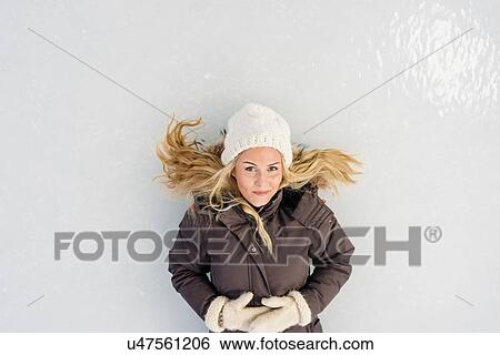 Stock Photograph - Overhead view of mid adult woman lying on ice looking at camera smiling. Fotosearch