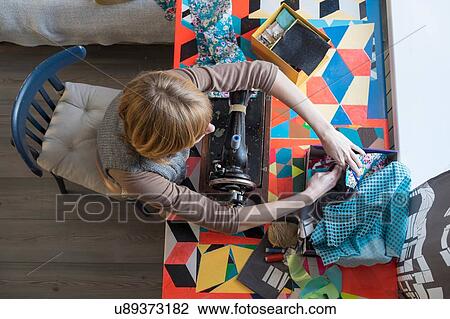 Stock Image - Overhead view of woman with vintage sewing machine selecting fabric. Fotosearch