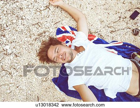 Overhead view of young man lying on back on beach on beach towel, looking away smiling, Costa Smeralda, Sardinia, Italy View Large Photo Image Stock Image - Overhead view of young man lying on back on beach on beach towel, looking away smiling, Costa Smeralda, Sardinia, Italy. Fotosearch