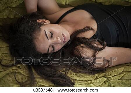 Stock Image - Overhead view of young woman lying on back, hand behind head looking away. Fotosearch