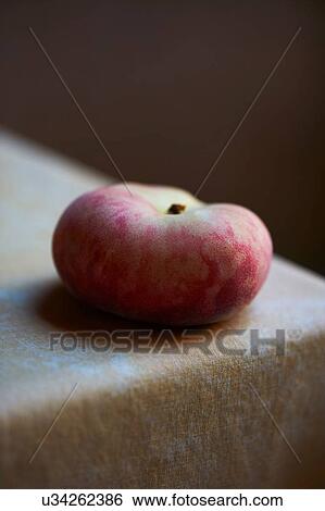 Stock Photograph - Peach on corner of cloth covered table. Fotosearch